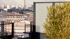 A view from a window overlooking a cityscape with the Eiffel Tower in the distance, a variety of buildings, and a potted plant in the foreground.