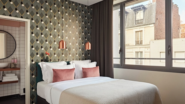 A modern hotel room with a large bed, a bathroom with a mirror and sink, and a view of the city through a window.