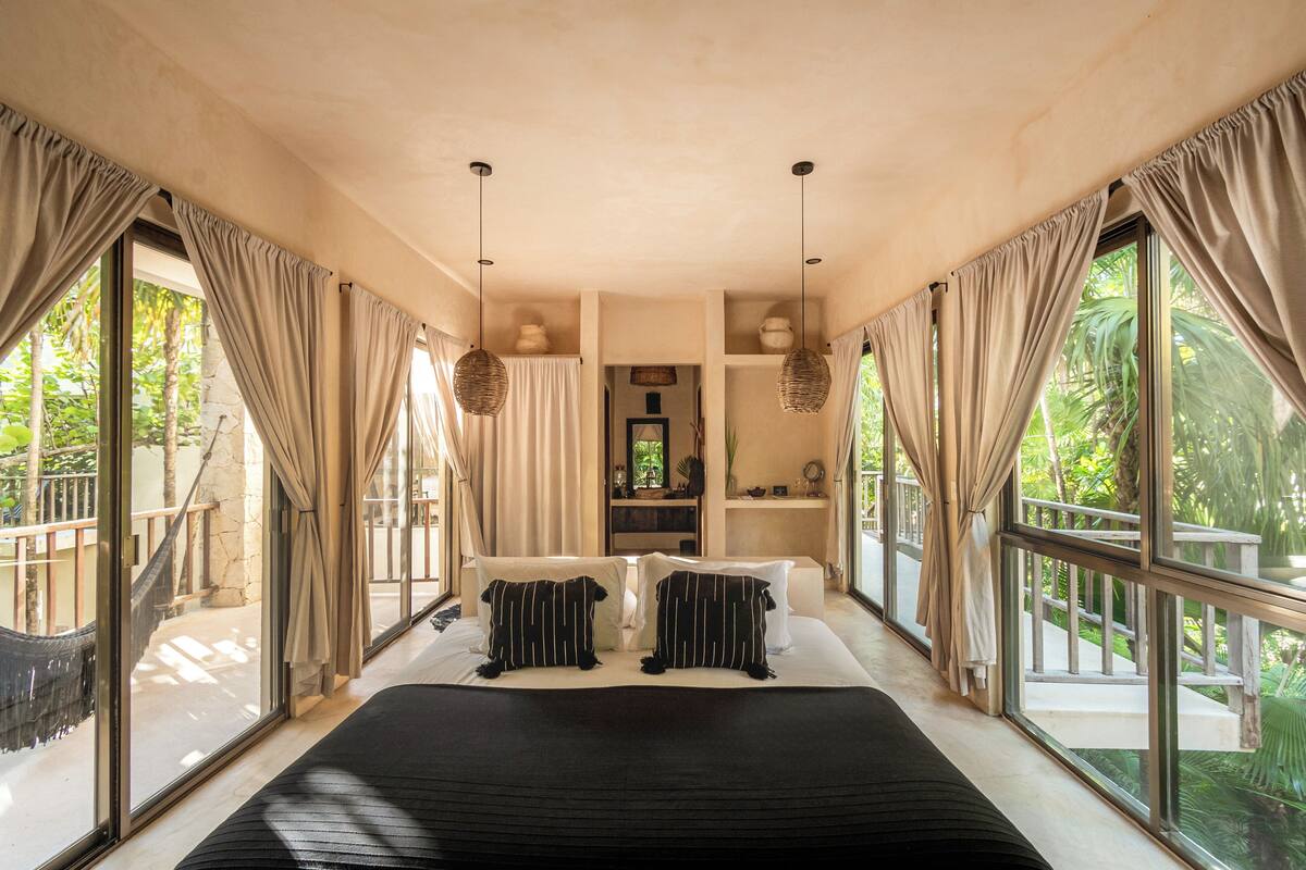 A spacious bedroom with a large bed, two hanging baskets, and a view of a balcony with a hammock.