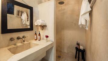 A bathroom with a large sink, a mirror, a shower, and towels on a rack.