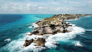 A coastal landscape with rocky cliffs, clear turquoise waters, and a distant town with buildings and greenery.