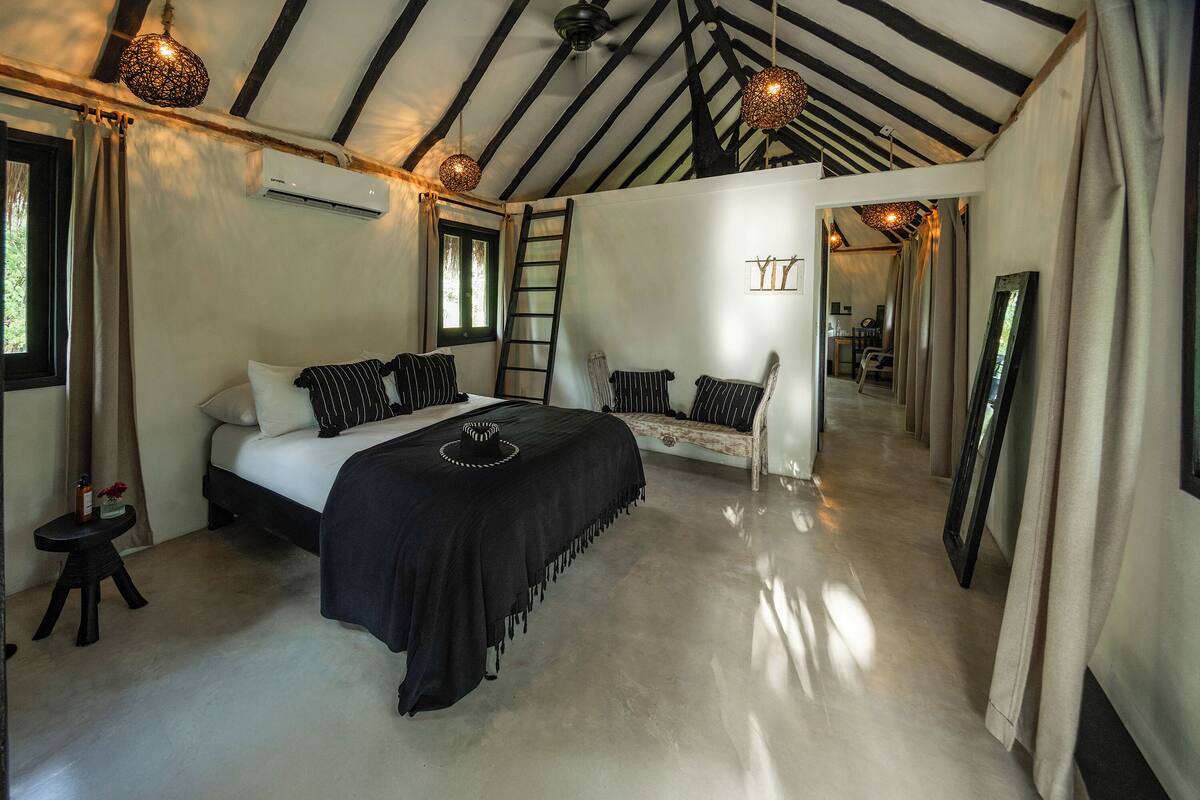 A bedroom with a bed, a sofa, a ladder, and a mirror.
