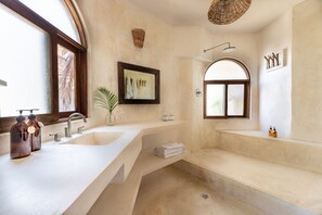 A modern bathroom with a large sink, two mirrors, a shower, and a window.