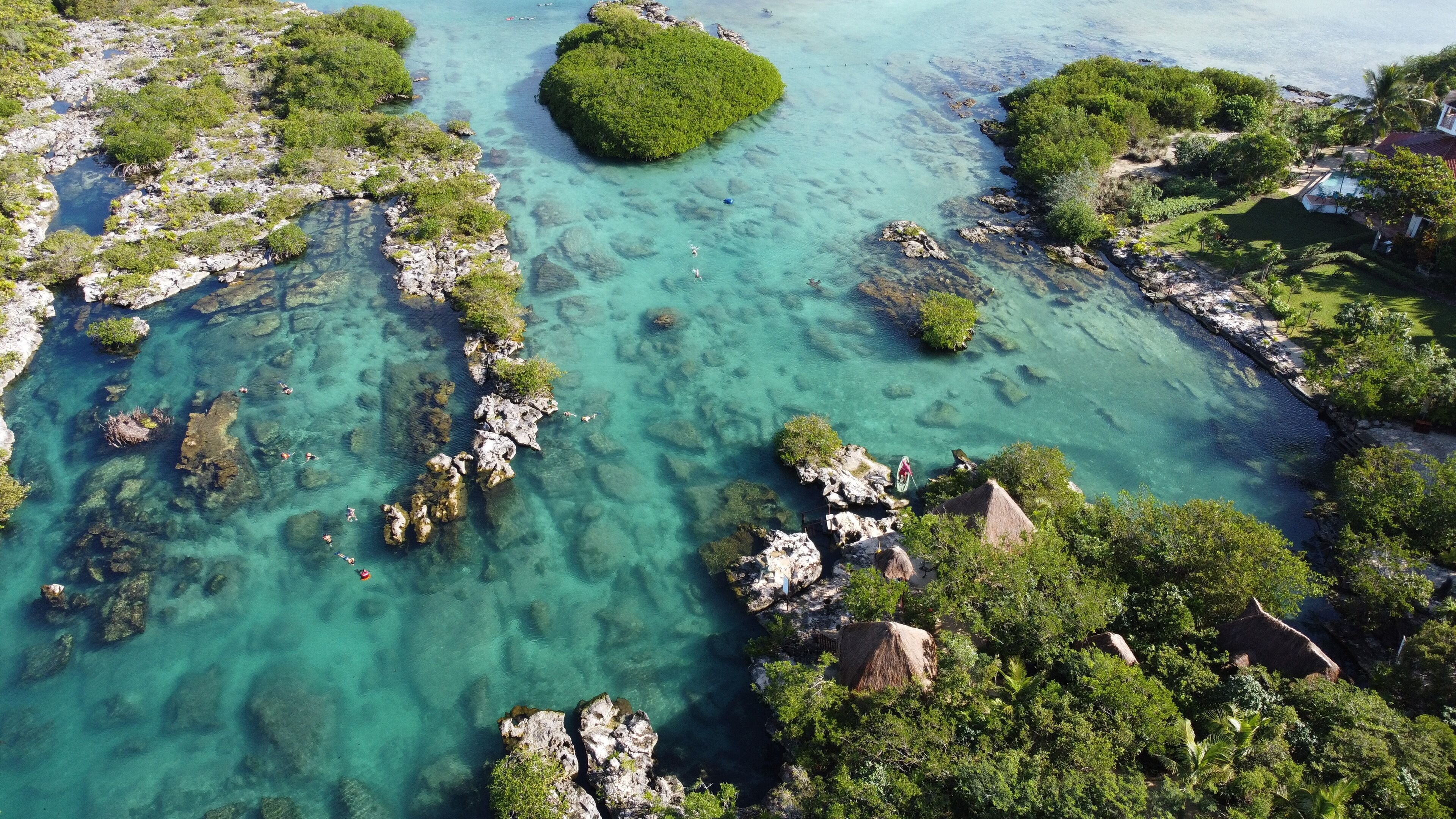 An aerial view of a coastal area with clear turquoise waters, rocky outcrops, and lush greenery.