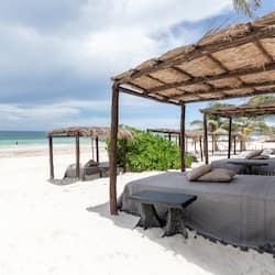 Relax under the shade of our beachside structures, featuring comfortable beds with plush bedding.