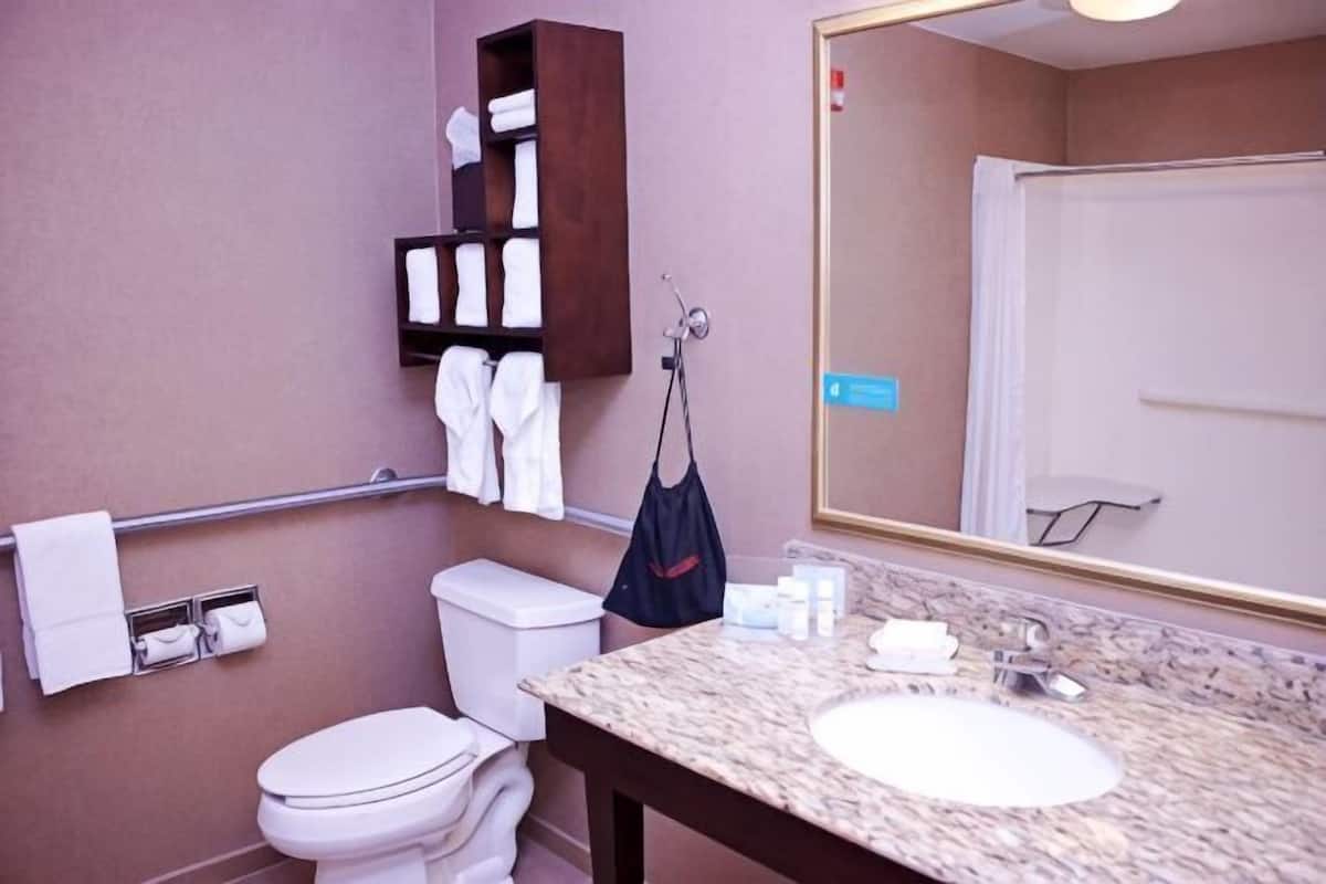 A bathroom with a toilet, sink, mirror, towel rack, and a small shelf with toiletries.