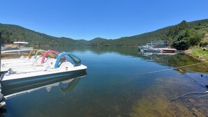 Un lago tranquilo con barcos amarrados a la orilla, rodeado de colinas boscosas.
