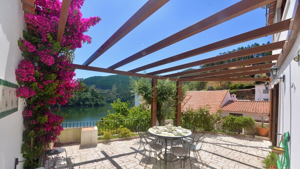 Un patio techado con una mesa y sillas, con vistas a un río y colinas.