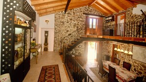 Un interior rústico con pared de piedra, vigas de madera, una escalera y un comedor con una mesa dispuesta para cuatro.