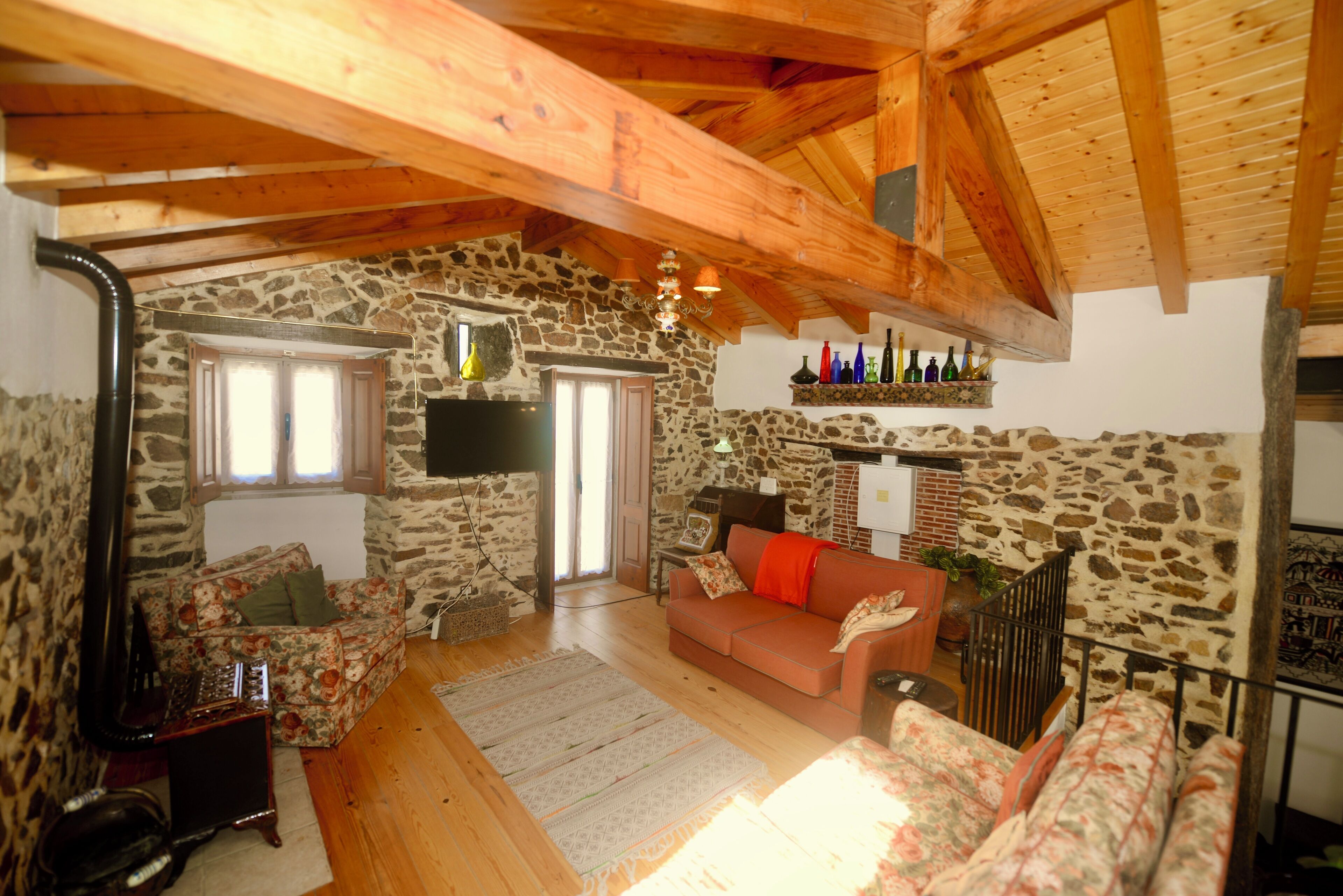 Una sala de estar acogedora con pared de piedra, vigas de madera, un sofá, una mesa de centro y una chimenea.
