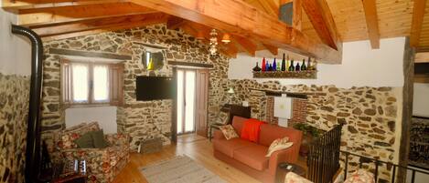 Una sala de estar acogedora con pared de piedra, vigas de madera, un sofá, una mesa de centro y una chimenea.