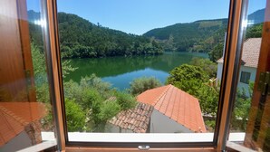 Vista a través de una ventana de un lago rodeado de colinas boscosas, con un edificio de techo rojo al frente.