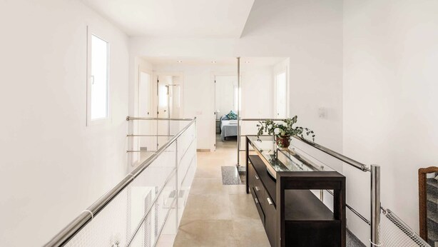 A modern, well-lit hallway with a glass railing, a wooden bench, and a potted plant. - Villa Catalina (Nerja)