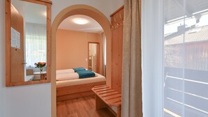 A bedroom with a bed, a wooden bench, a mirror, and a view of the outside. - Pension Freiheit (Pfronten)