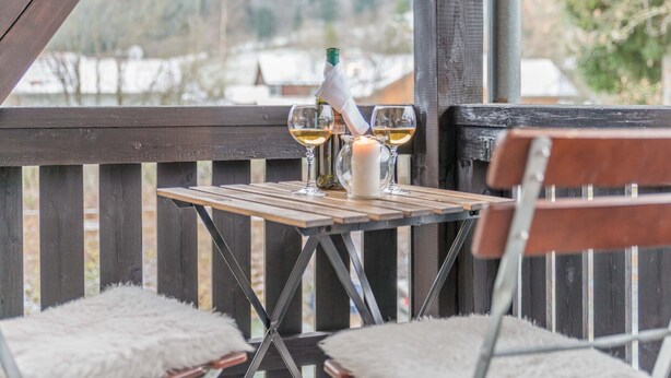 A wooden table with two glasses of white wine, a candle, and a bottle on a balcony with a view of a snowy landscape. - Pension Freiheit (Pfronten)