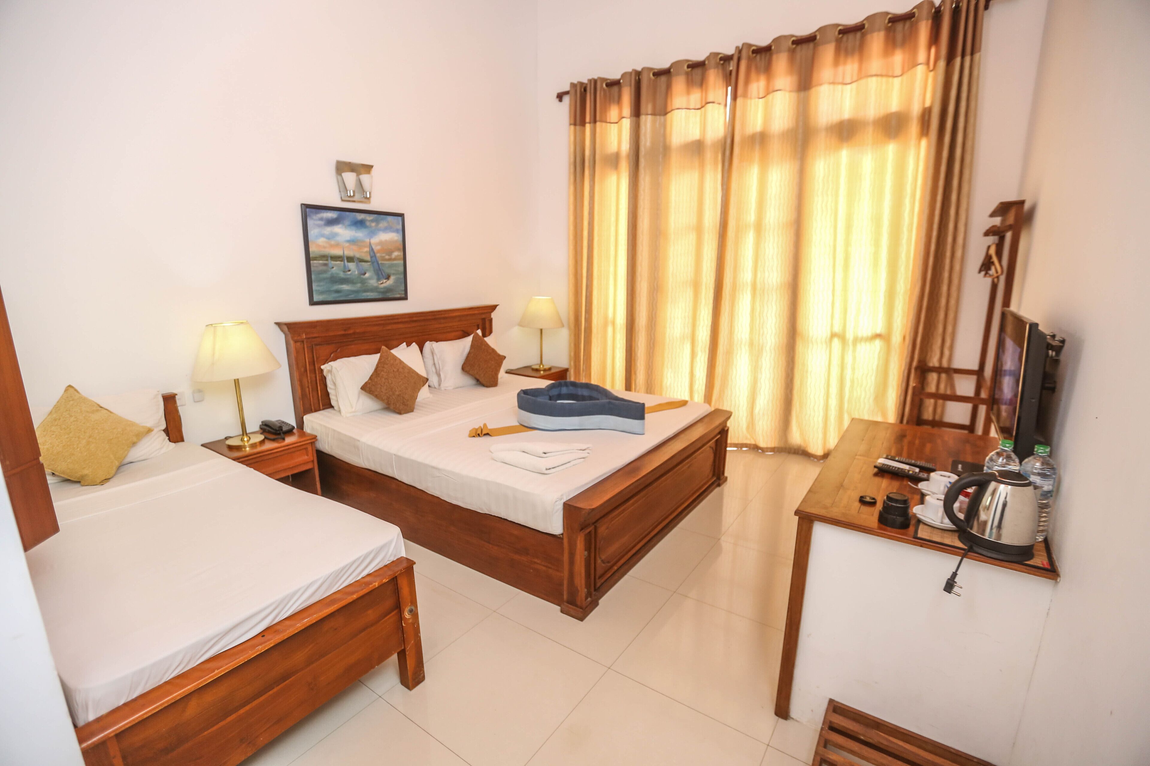 A hotel room with two single beds, a wooden headboard, a small desk with a chair, a coffee maker, and a painting on the wall.