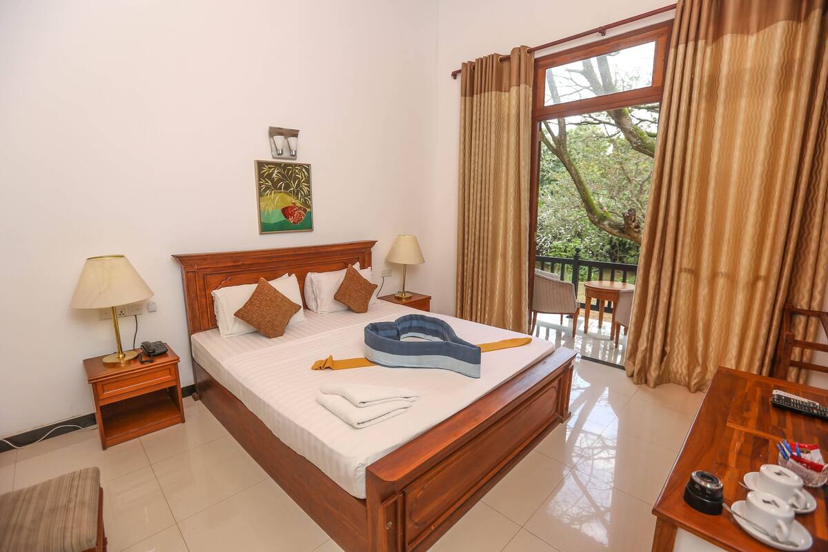 A hotel room with a bed, bedside tables, a desk, a chair, and a balcony with curtains.