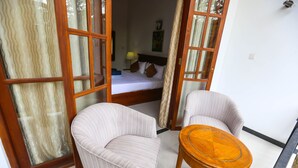 Ein Zimmer mit einem Bett, zwei Stühlen, einem kleinen Holztisch und einem großen Fenster mit Vorhängen.