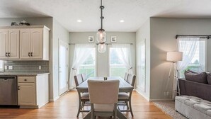 A modern kitchen with white cabinets, a dining table with chairs, and a pendant light. - CLEAN Updated & Spacious Family Home! (Elkhorn)