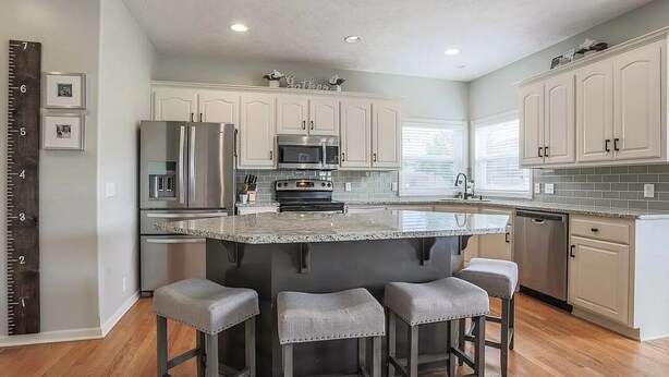 A modern kitchen with white cabinets, stainless steel appliances, and a central island with bar stools. - CLEAN Updated & Spacious Family Home! (Elkhorn)