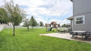 A backyard with a playset, a small tree, and a patio area with a table and chairs. - CLEAN Updated & Spacious Family Home! (Elkhorn)
