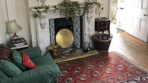 Una sala de estar con chimenea, sofás verdes y rojos, un tapete estampado y un espejo en la pared.