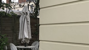 Una bañera blanca llena de flores de colores, ubicada sobre grava junto a una valla de madera y una pared blanca.