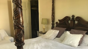 Una cama con dosel adornada con tallas elaboradas, un edredón blanco y varias almohadas.