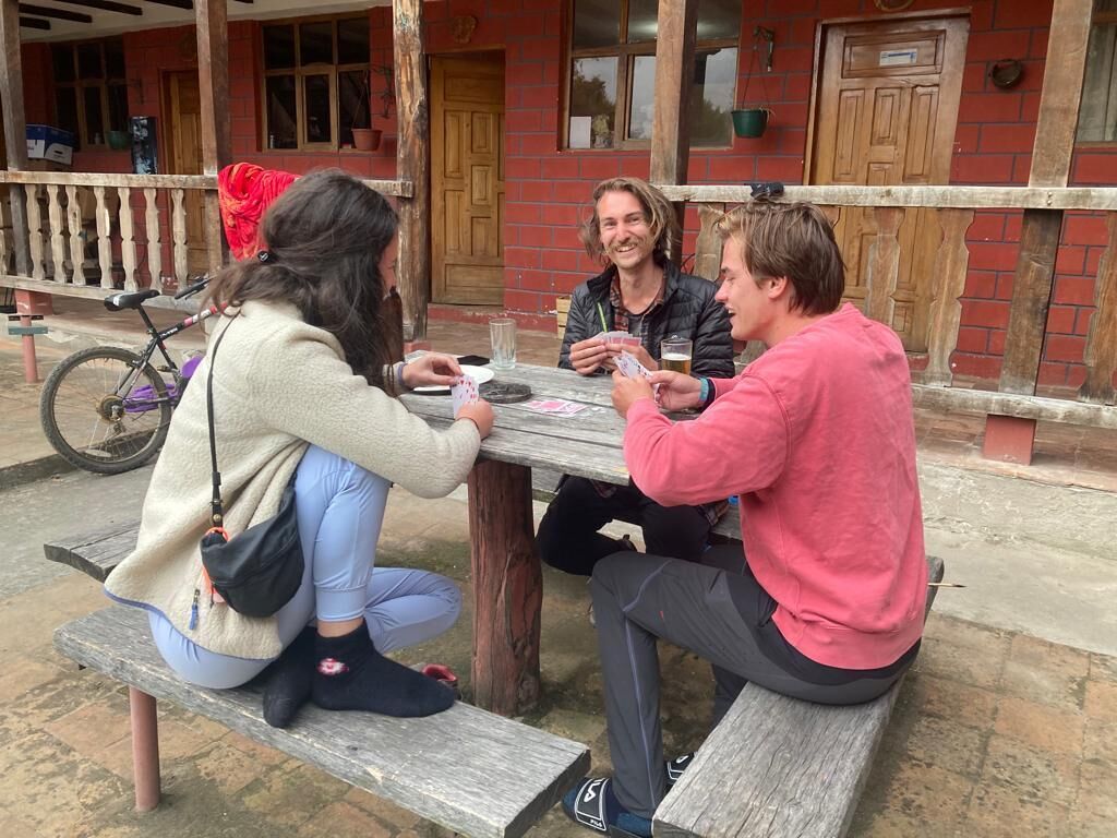 Tres personas sentadas en una mesa de madera al aire libre, jugando a las cartas.