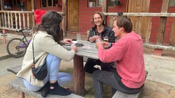 Tres personas sentadas en una mesa de madera al aire libre, jugando a las cartas.