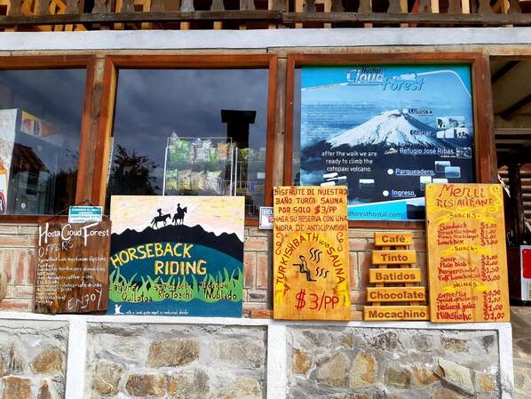 A hostel with a sign offering horseback riding, a menu board, and a poster advertising the Hostel Cloud Forest. - Hostal Cloud Forest (Chugchilan)