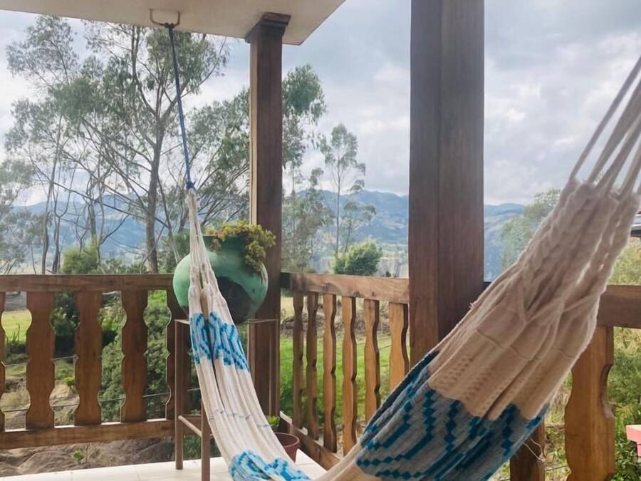 A hammock on a balcony with a view of trees and mountains.