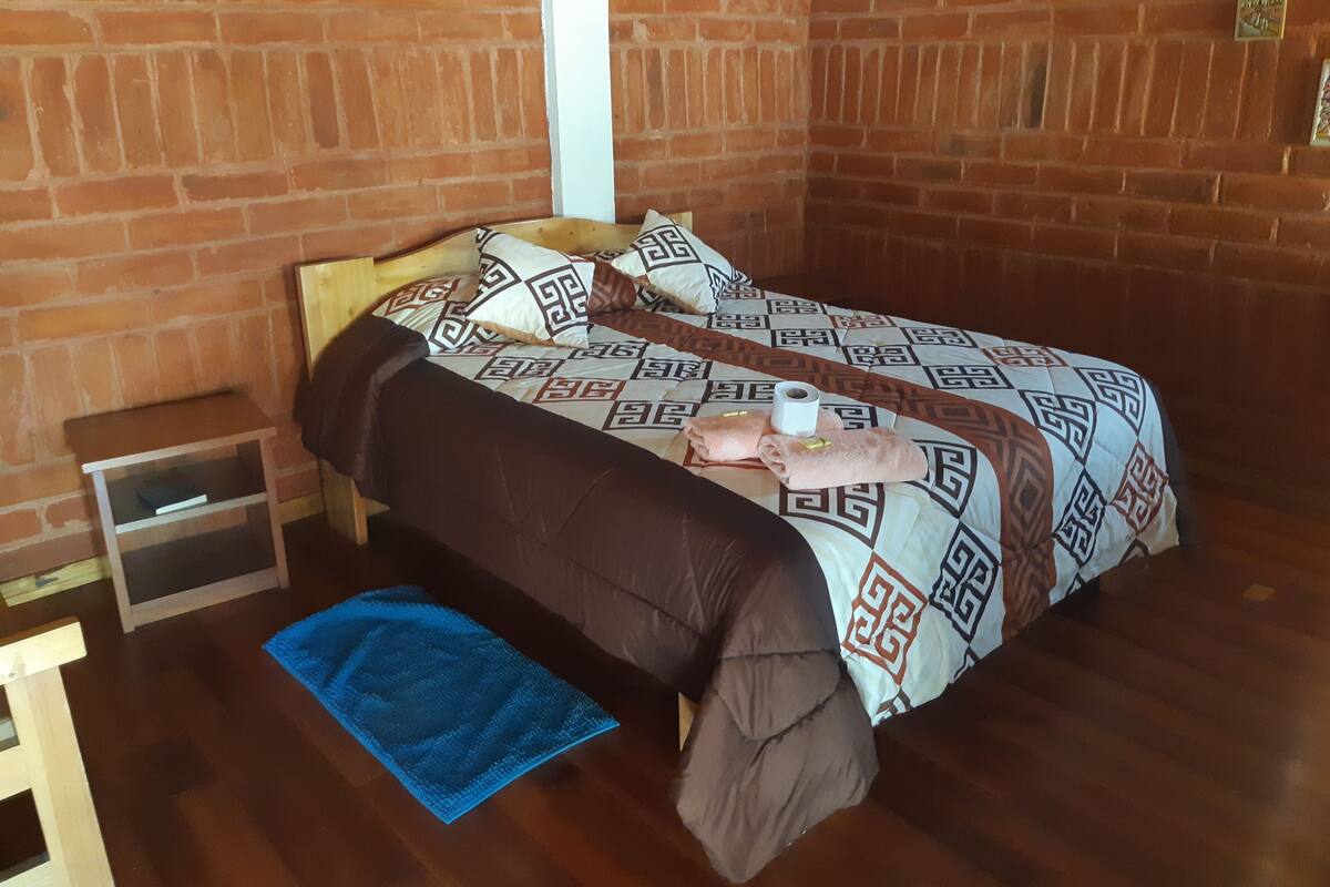 A single bed with a patterned bedspread, a blue towel, and a small bedside table with a book.