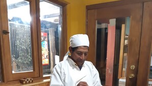 Une personne vêtue d'un uniforme de chef blanc se tient devant une table sur laquelle se trouvent un gâteau et un pot de crème.