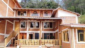 Une maison en bois à deux étages, dotée d’un balcon, d’un revêtement de sol en pierre et d’un escalier en bois.