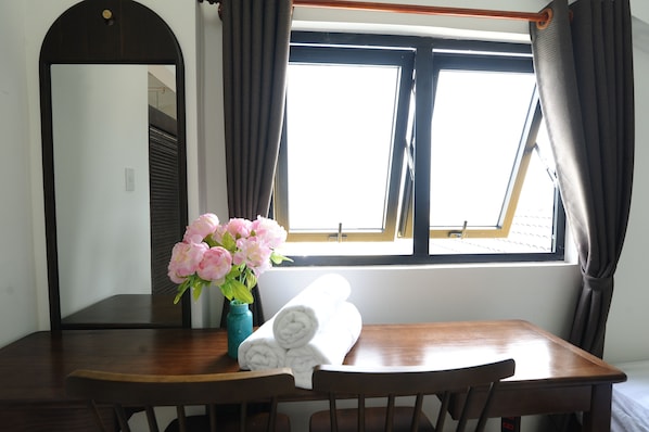 A room with a wooden table, a rolled white towel, and a vase of pink flowers.