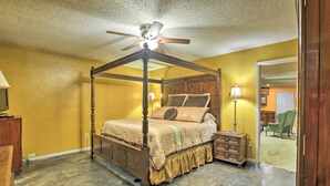 Ein Bett mit Baldachin, dessen Gestell aus Holz besteht, ein Deckenventilator, ein Nachttisch mit Lampe sowie eine Holzkommode.