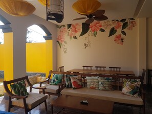 Ein Essbereich mit einem hohen Deckenventilator, einer Wandmalerei mit Blumen und einer gelben Außenwand.