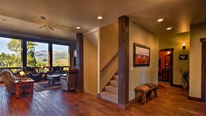 Un amplio salón con piso de madera, una escalera y un ventanal con vistas al exterior.