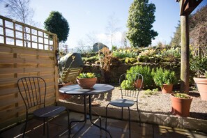 A patio with two metal chairs and a round table, surrounded by potted plants and a wooden fence. - Birdsong Cottage B&B (Chathill)