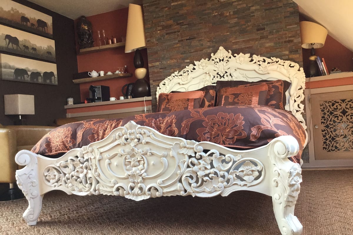 A bed with ornate white carvings, a patterned bedspread, and a brick wall in the background.