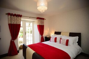A bedroom with a large bed, red and white curtains, a chandelier, and a view of the outdoors. - Birdsong Cottage B&B (Chathill)