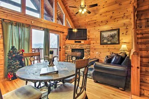 L’intérieur chaleureux d’un chalet avec une cheminée en pierre, des murs en bois, une table à manger ronde et un canapé confortable.