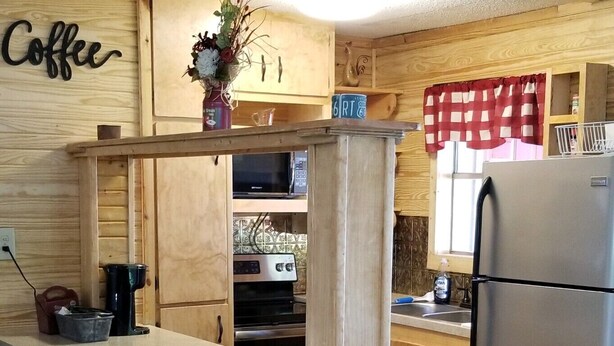 Een keuken met houten kasten, een centraal eiland, een koelkast en een bord met de tekst 'coffee' aan de muur.