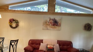 Een woonkamer met een rode leren bank, een schilderij van een rode schuur, en een houten plafond met dakramen.