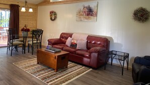 Een gezellige woonkamer met een rode leren bank, een houten salontafel en een eethoek met een tafel en stoelen.