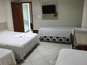 Habitación de hotel con dos camas individuales, un televisor montado en la pared y una pequeña mesa con una silla.
