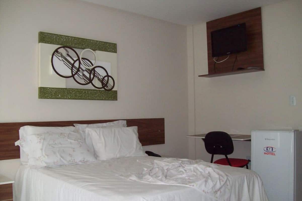 Una habitación de hotel con cama, escritorio, silla, televisor y minibar.
