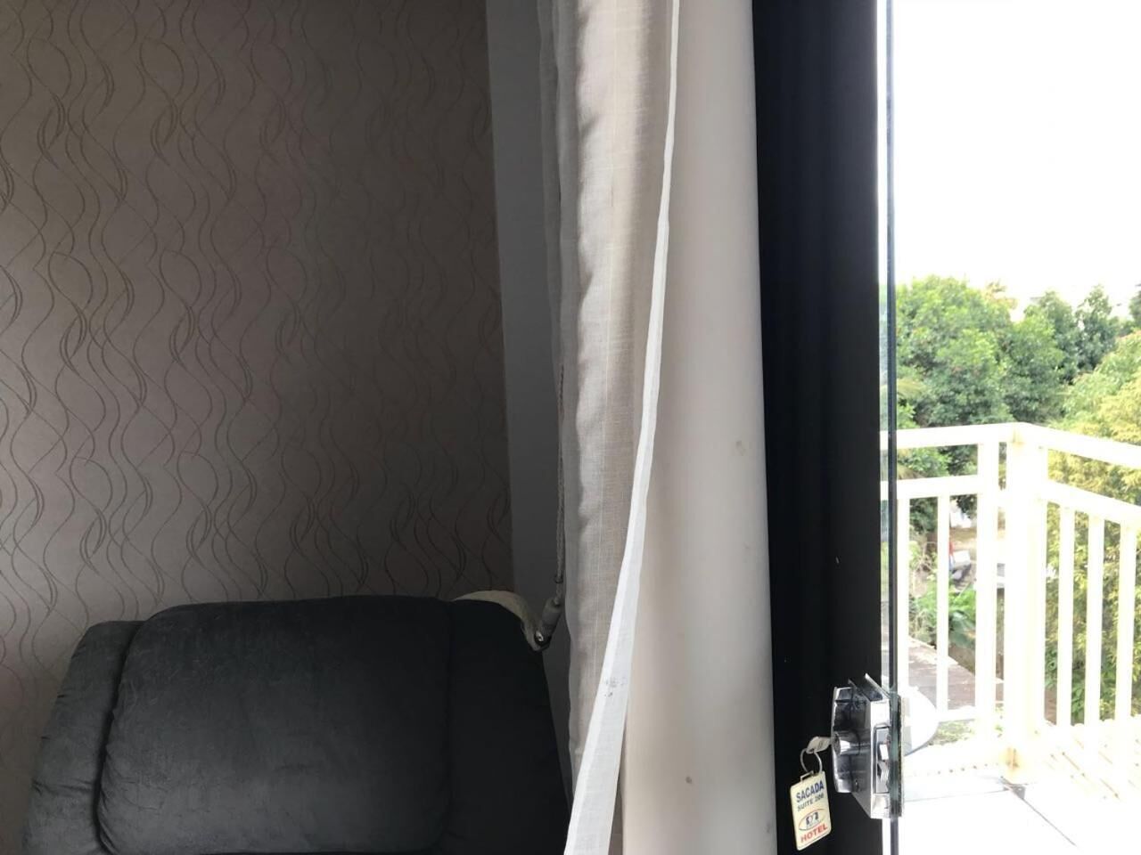 A room with a patterned wallpaper, a black chair, and a white curtain.