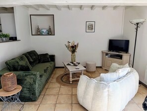 Una sala de estar con un sofá verde, un sillón blanco, una mesa de centro, un televisor y una estantería.